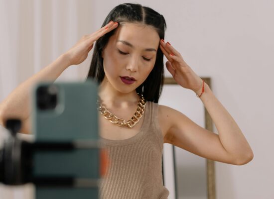 Person posing in front of smartphone, hands near head, indoors.