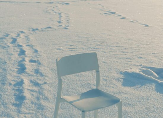 A single chair sits alone on a snowy landscape.