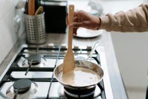 Person stirring sauce in pan on stove with spatula.