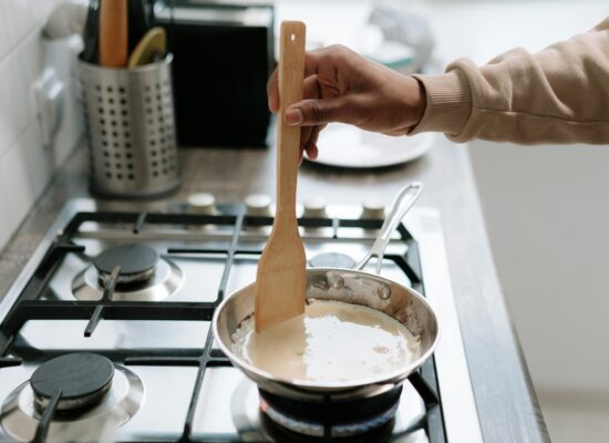 Person stirring sauce in pan on stove with spatula.
