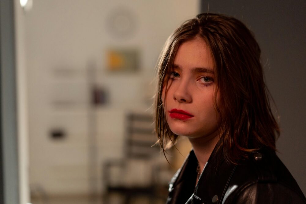 Person with red lipstick looks serious, wearing a black jacket.