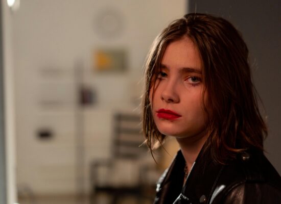 Person with red lipstick looks serious, wearing a black jacket.