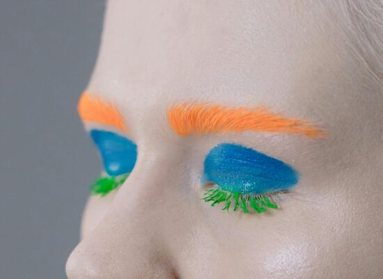 Bright orange eyebrows, blue eyeshadow, and green mascara on eyelashes.