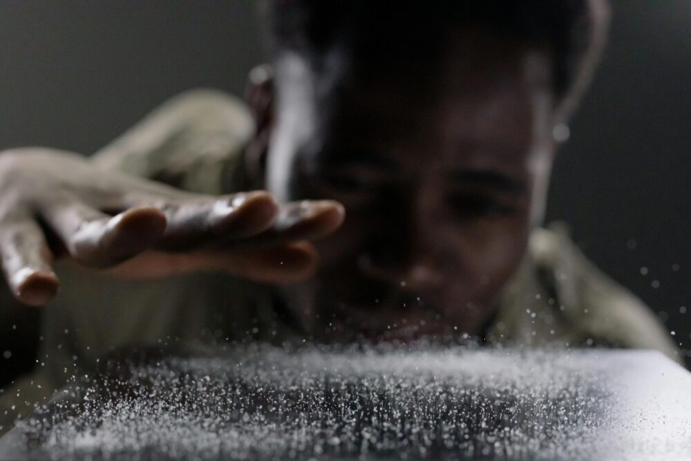 Person blowing on surface, causing particles to scatter dramatically.