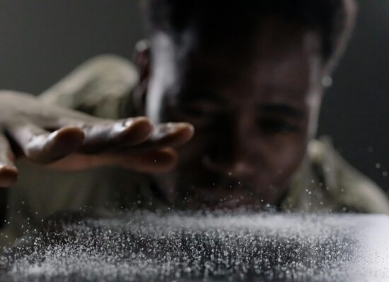 Person blowing on surface, causing particles to scatter dramatically.
