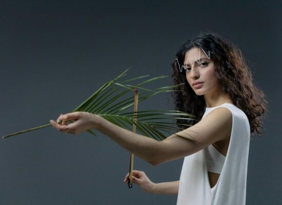 Person holding palm leaf, wearing white outfit, creative makeup.