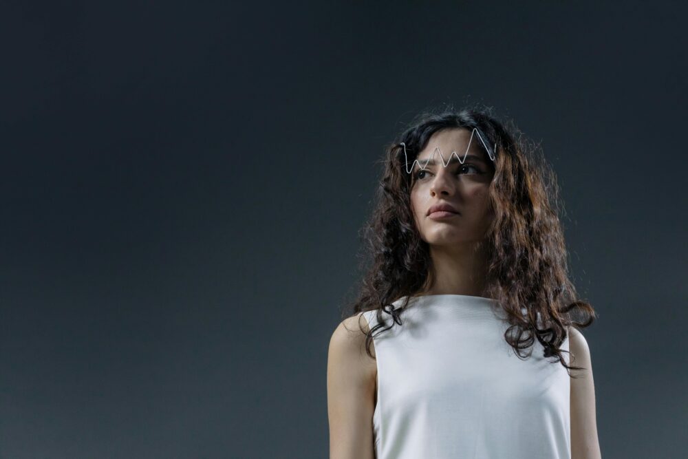 Person with wavy hair wearing white, zigzag accessory on forehead.