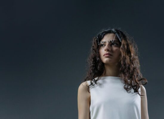 Person with wavy hair wearing white, zigzag accessory on forehead.