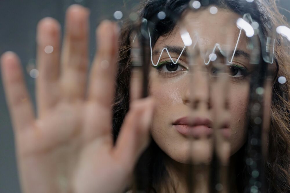 Person behind glass with hand raised, reflections and light distortions.