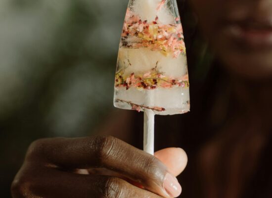 Hand holding a popsicle with flowers frozen inside, outdoors.