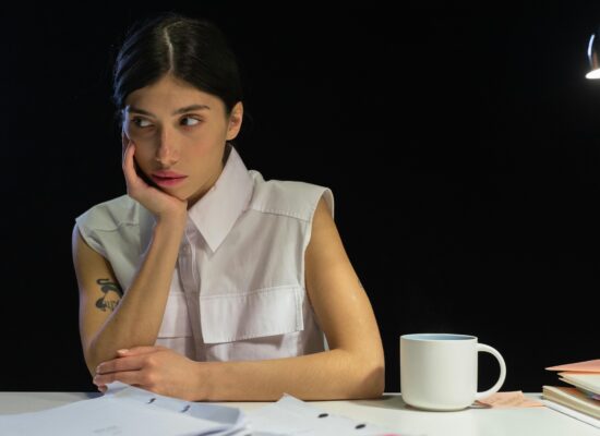 Person looking away from camera, resting chin on hand, with papers and mug.