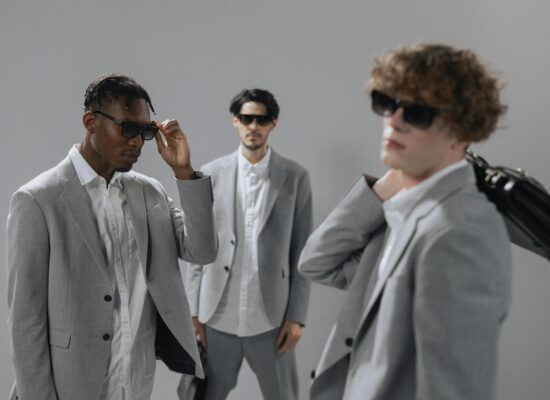 Three men in grey suits and sunglasses pose against a grey background.