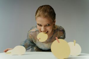 Person biting a yellow paper circle with a pink square.