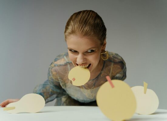 Person biting a yellow paper circle with a pink square.