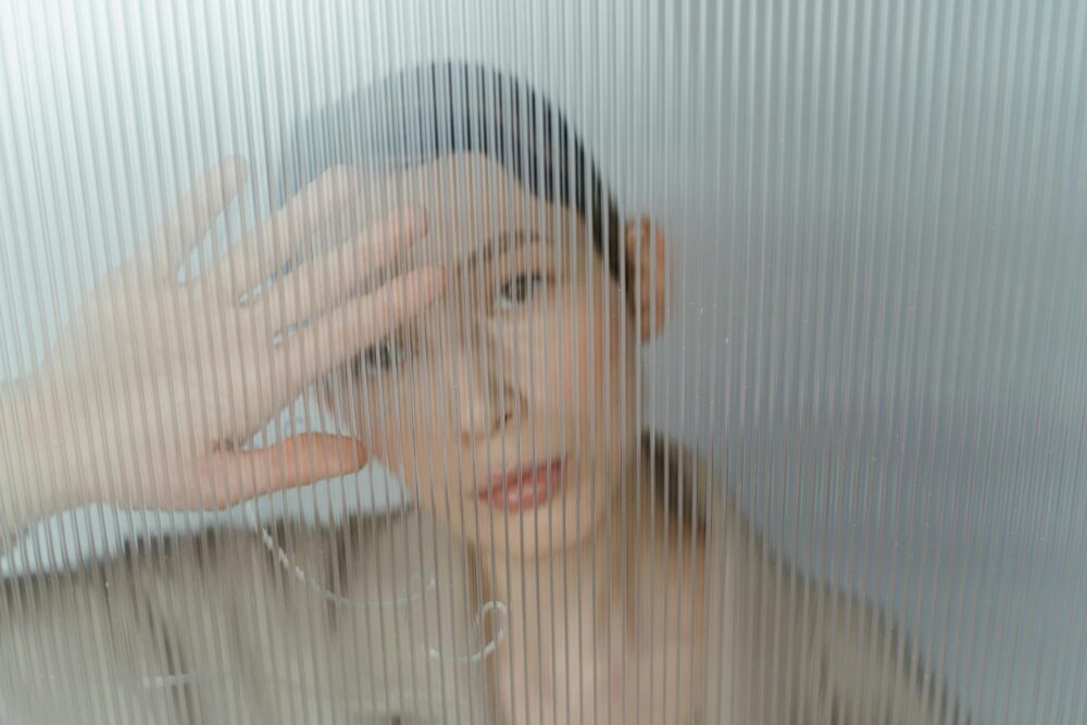Person behind frosted glass, hand obscuring face, looking out.