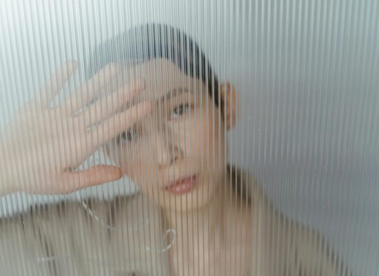 Person behind frosted glass, hand obscuring face, looking out.