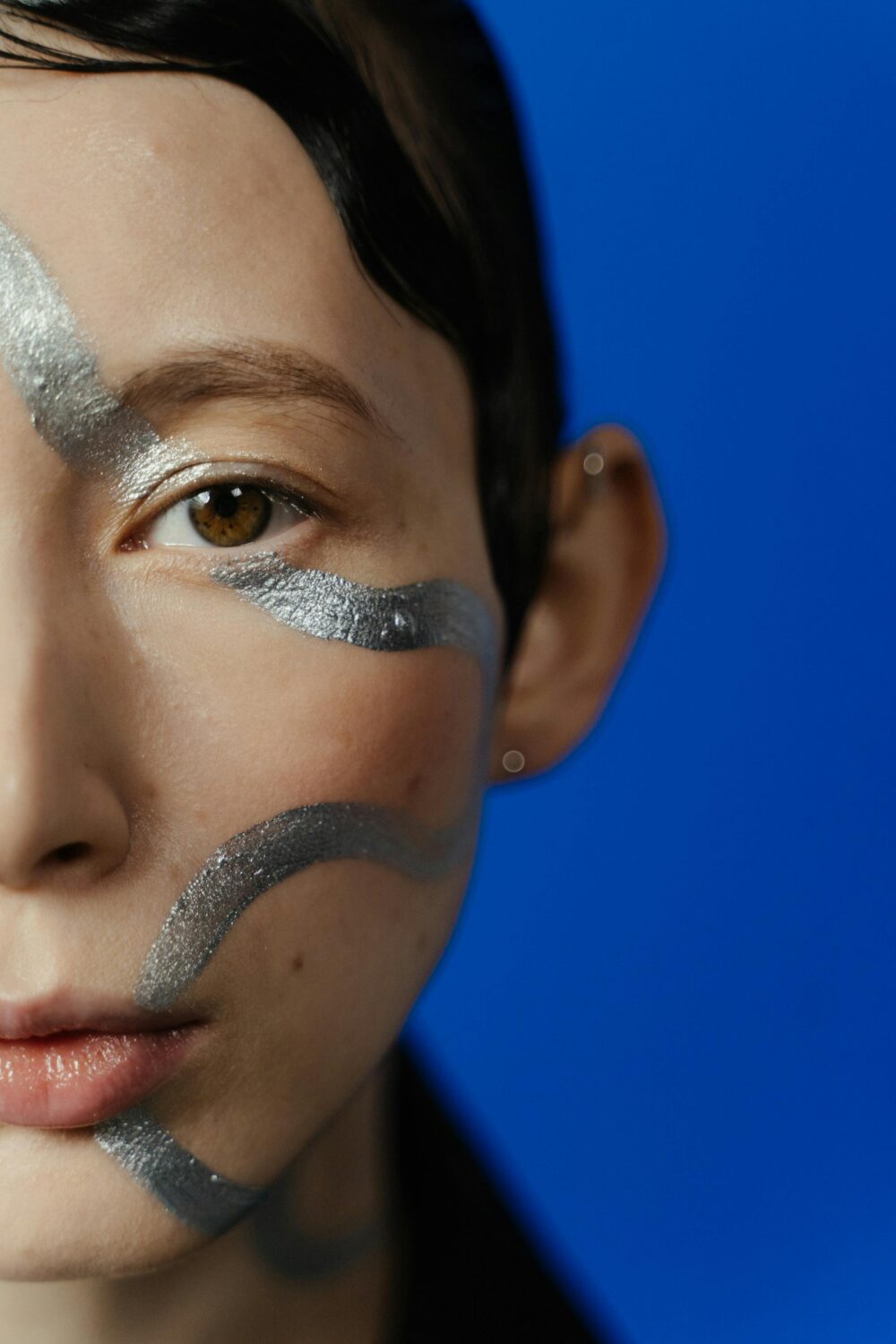 Close-up of a face with silver body paint against a blue background.