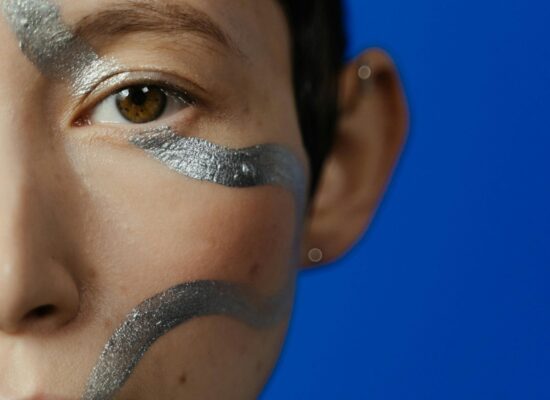 Close-up of a face with silver body paint against a blue background.