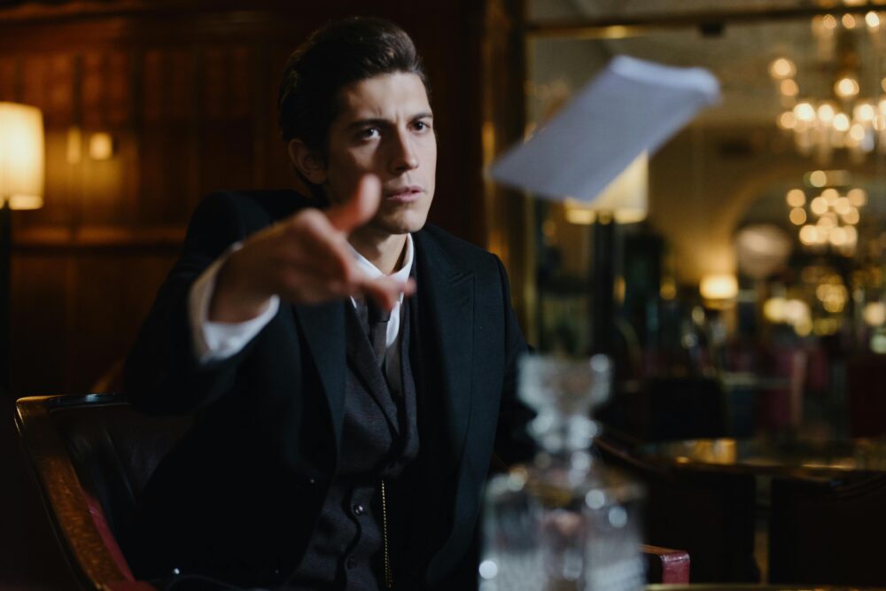 A man in a suit throws a paper in a dimly lit room.
