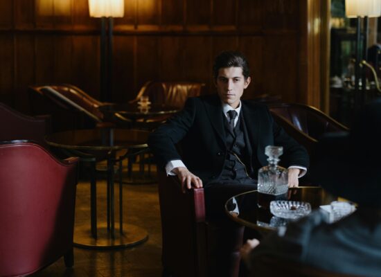Man in suit sits in a dimly lit lounge with decanter.