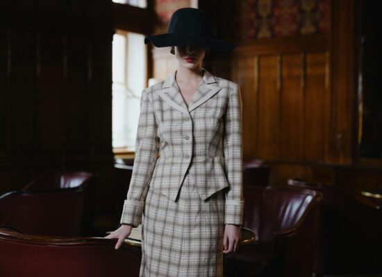 A person in a plaid suit and wide-brimmed hat stands in a dimly lit room.