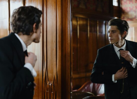 Man in a suit adjusts his tie in a mirror.