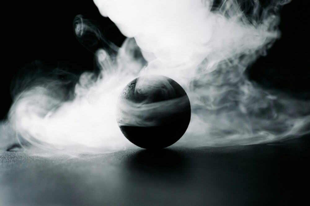 A dark sphere surrounded by swirling white smoke on black background.