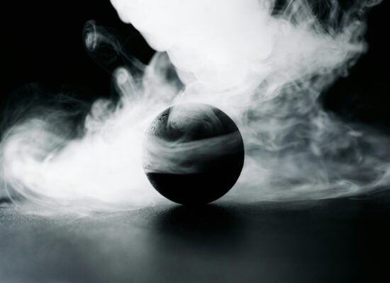 A dark sphere surrounded by swirling white smoke on black background.