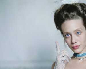 A person in vintage attire with a feather in their hair.