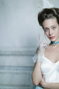 A person in vintage attire with a feather in their hair.