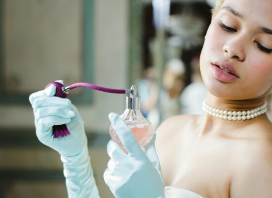 Person in light blue gloves sprays perfume from a vintage bottle.