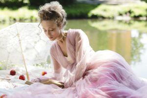 A person in a pink dress reads a book by a lake.