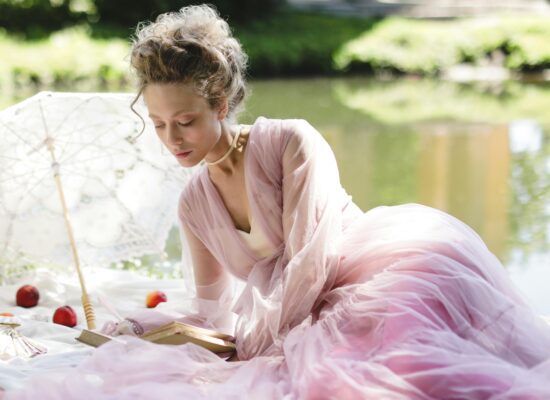 A person in a pink dress reads a book by a lake.