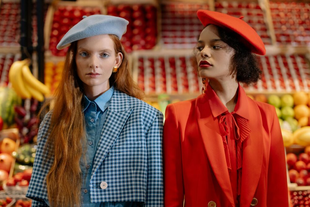 Two people in berets stand in front of a fruit stand.