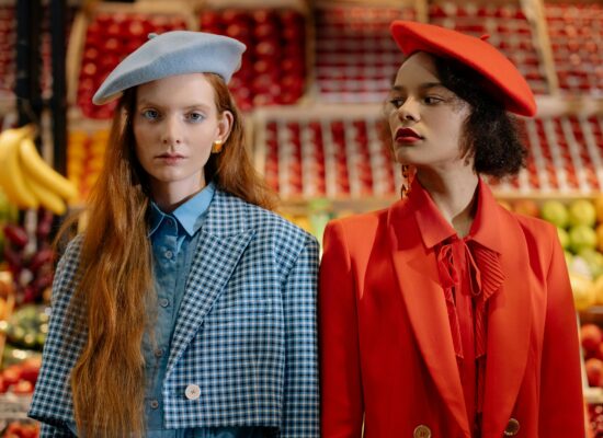Two people in berets stand in front of a fruit stand.