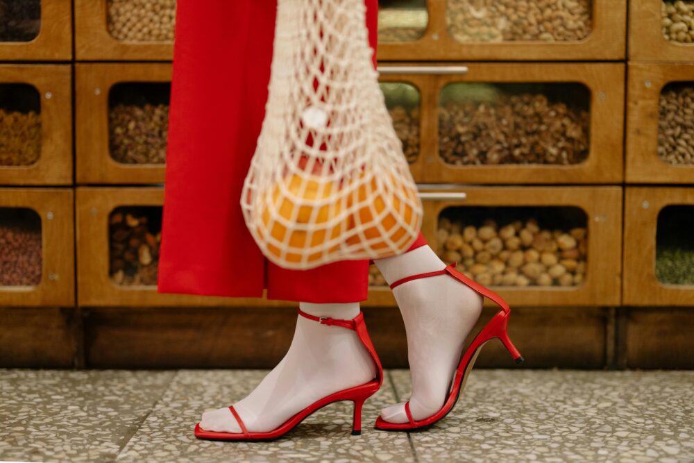 Red shoes and a bag of oranges in front of nut dispensers.