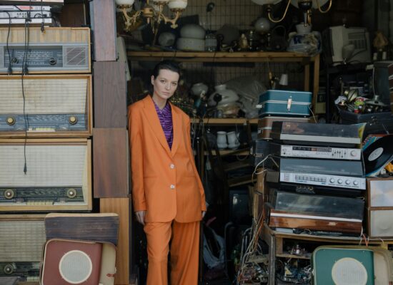 Person in orange suit stands amidst vintage electronics and luggage.