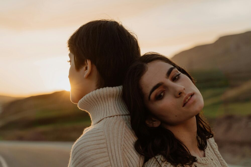 Two people leaning on each other at sunset with warm light.
