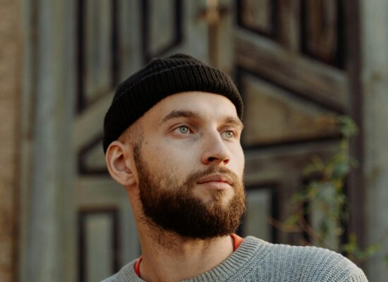 Person wearing a knit sweater and beanie, standing outdoors, thoughtful.