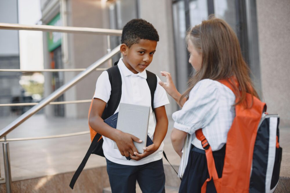 Two children with backpacks and books outside a building.
