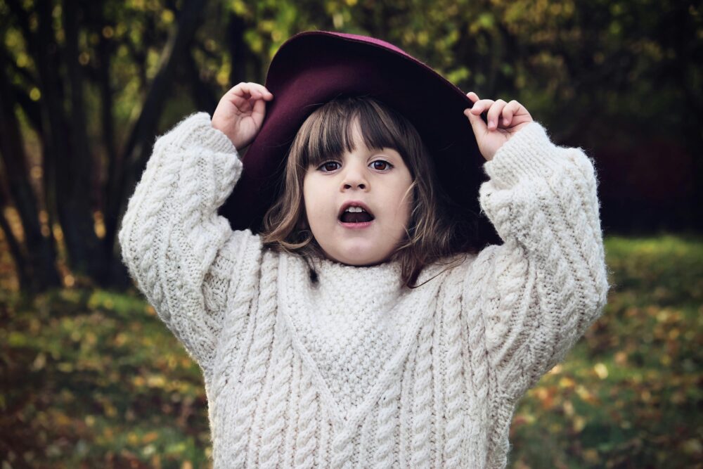 A child in a cream sweater and burgundy hat looks surprised.