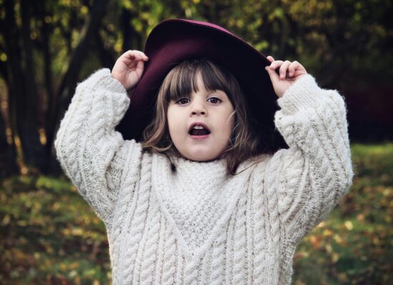 A child in a cream sweater and burgundy hat looks surprised.