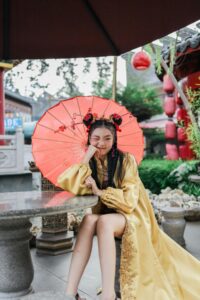 A person in a golden dress with a red umbrella in a garden.