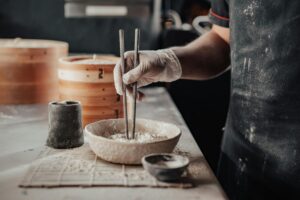 Gloved hand using chopsticks in flour, preparing food, kitchen scene.