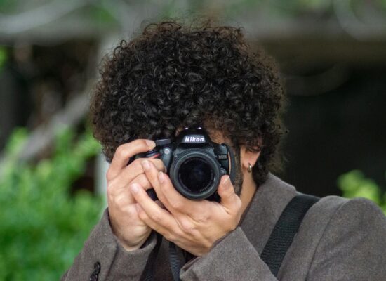 Person with curly hair taking a photo with a Nikon camera.