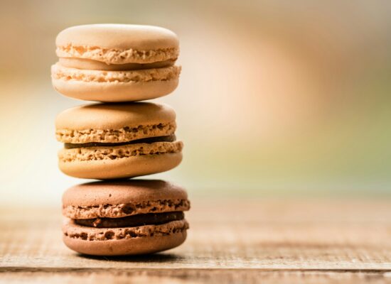 Three stacked macarons on a wooden surface, blurred background.
