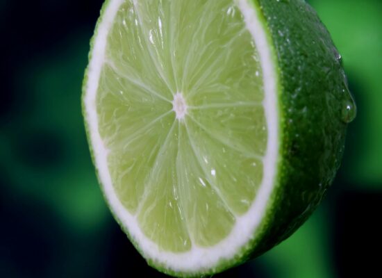 Close-up of lime slice with juice droplet, green background.