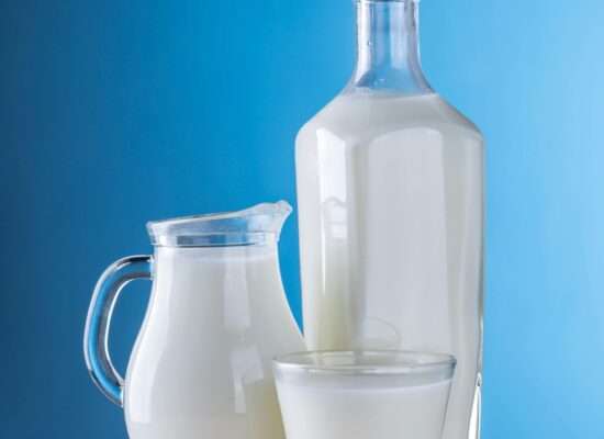 Glass bottle, jug, and cup filled with milk, blue background.