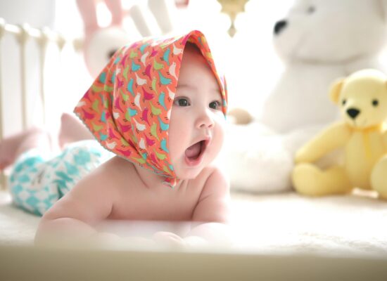 A baby wearing a colorful bandana lies on its stomach with toys.
