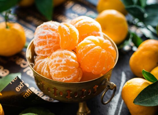 Peeled tangerines in a brass bowl surrounded by whole tangerines.